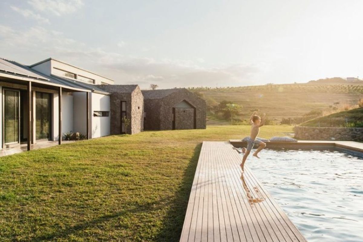 A modern outdoor pool area featuring extensive timber decking, stone-clad building structures, and a well-maintained lawn with scenic landscape views.