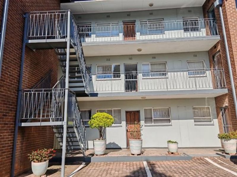 Rear elevation of a multi-story apartment building featuring external steel staircases, private balconies, and a paved ground-level parking area.