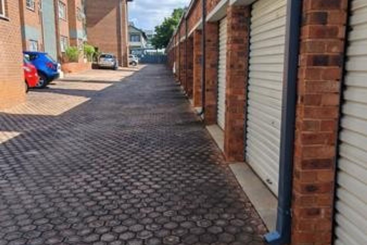 A view of a paved driveway lined with a row of brick-built garages featuring roller shutter doors.
