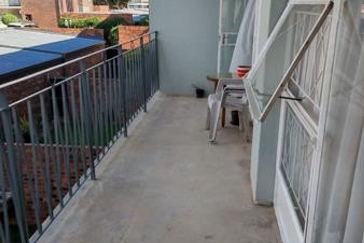 A functional apartment balcony featuring a metal balustrade, concrete flooring, and access via a sliding glass door, offering an outdoor space for relaxation.