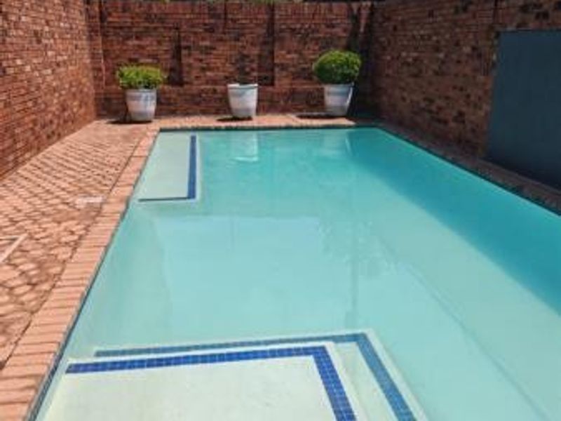 A private swimming pool area featuring a paved surround and enclosed by high brick boundary walls.