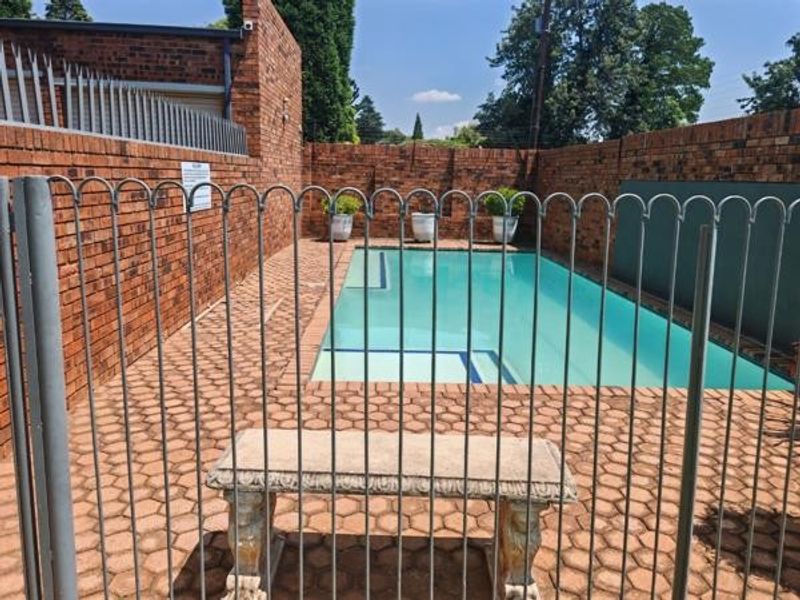 A private swimming pool area featuring a paved deck, enclosed by brick boundary walls and secure metal fencing.
