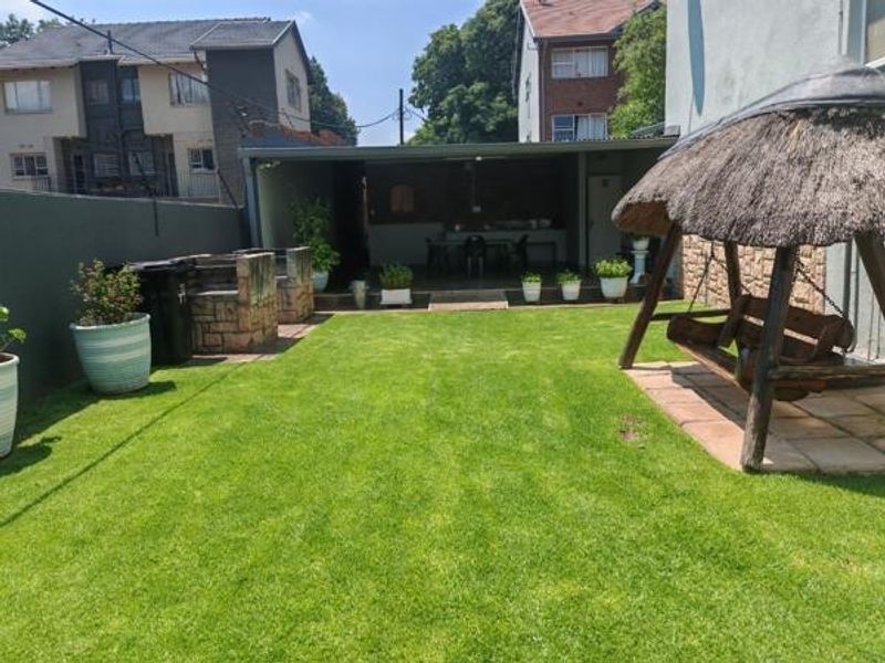 A private rear garden featuring a well-maintained lawn, a covered patio area, and a built-in braai, perfect for outdoor entertaining.
