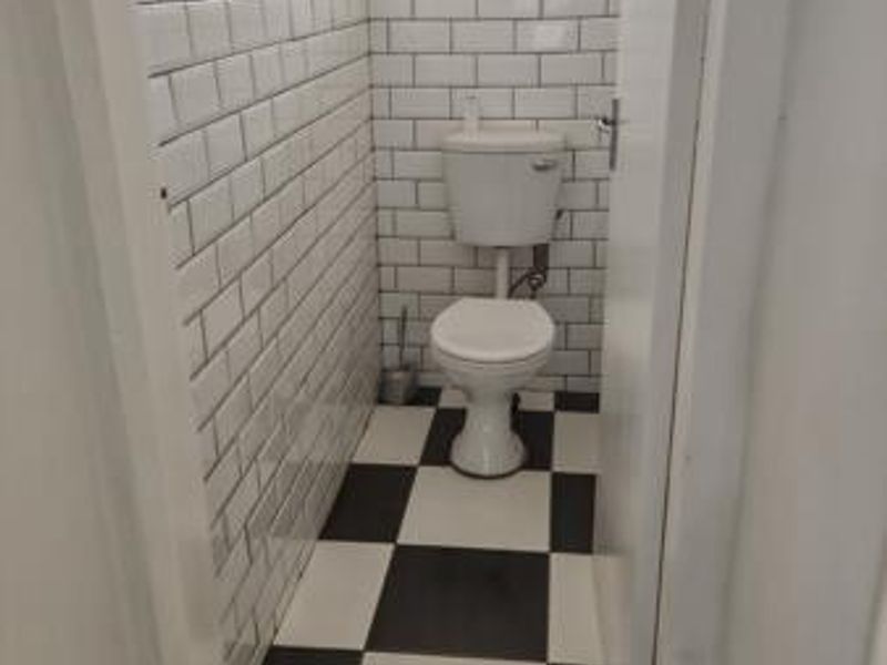 A compact bathroom featuring classic white subway wall tiles and a black and white checkered floor, complete with a standard toilet.