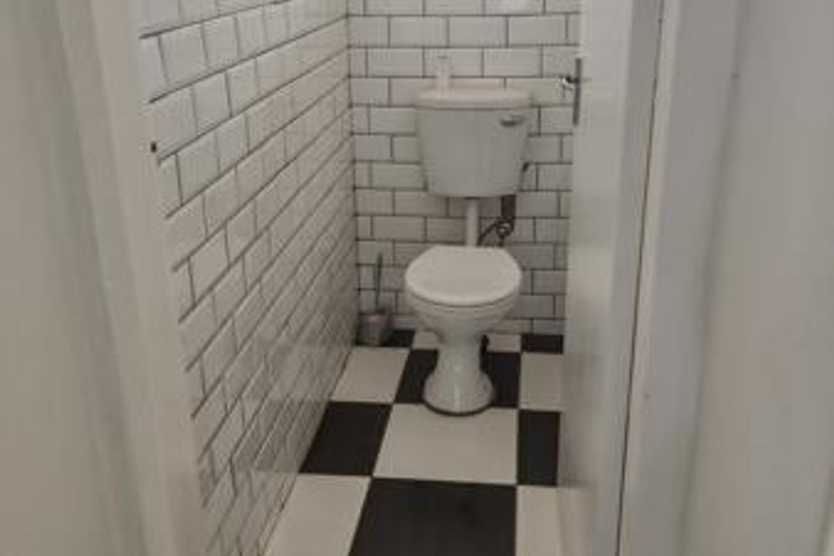 A compact bathroom featuring classic white subway wall tiles and a black and white checkered floor, complete with a standard toilet.
