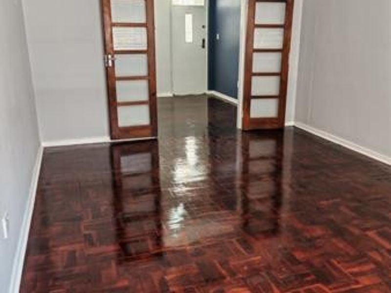 An empty living room featuring polished dark wood parquet flooring and double wooden doors with glass panels leading to an adjacent space.