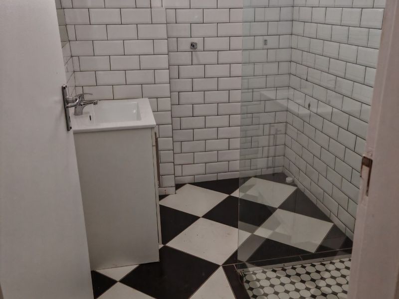 A modern bathroom featuring a vanity basin, a glass-enclosed shower, classic subway wall tiling, and a distinctive black and white checkered floor.