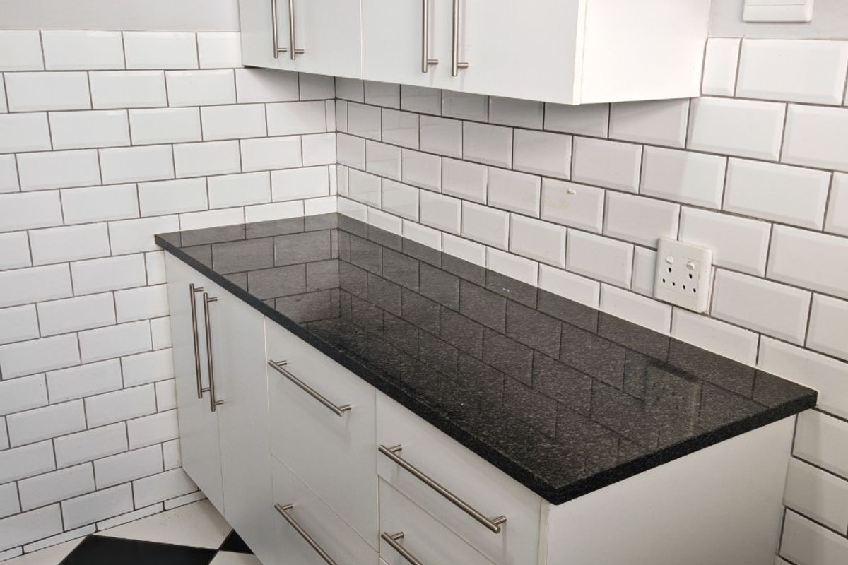 A clean, modern kitchen area featuring white cabinetry, black granite countertops, a classic subway tile backsplash, and distinctive black and white checkerboard floor tiles.