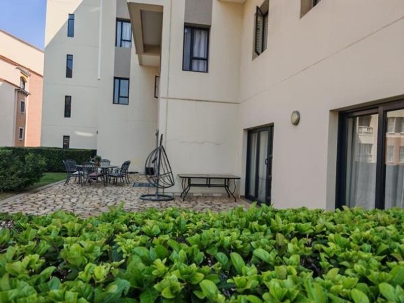 A rear exterior view of the townhouse featuring a paved patio area, sliding glass door access, and established garden hedging.