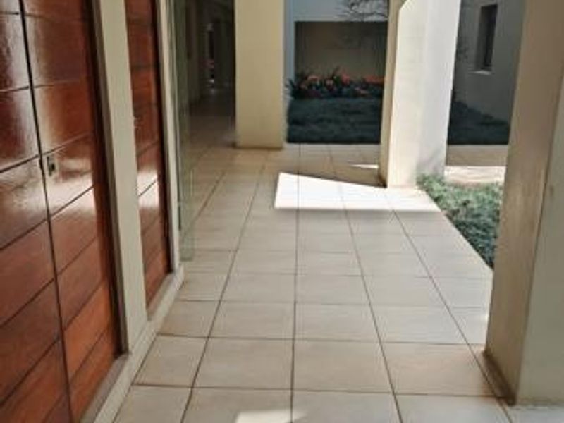 A clean, well-maintained hallway featuring tiled flooring and wooden wall paneling, leading towards an outdoor garden area.