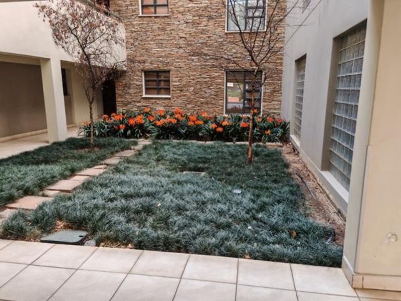 A well-maintained rear courtyard featuring stone-clad walls, glass block windows, a tiled patio area, and established garden landscaping.