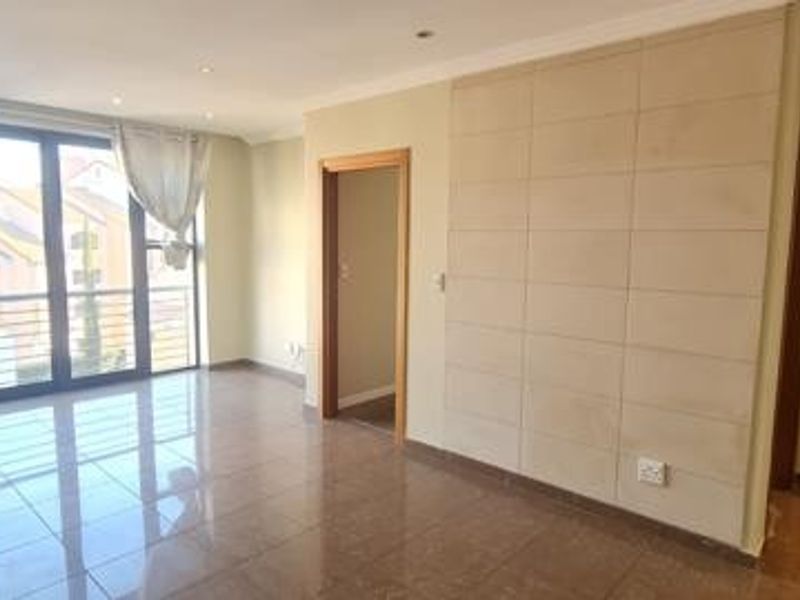 Spacious, light-filled living area featuring polished tiled floors, a modern feature wall, and large sliding doors leading to a balcony.