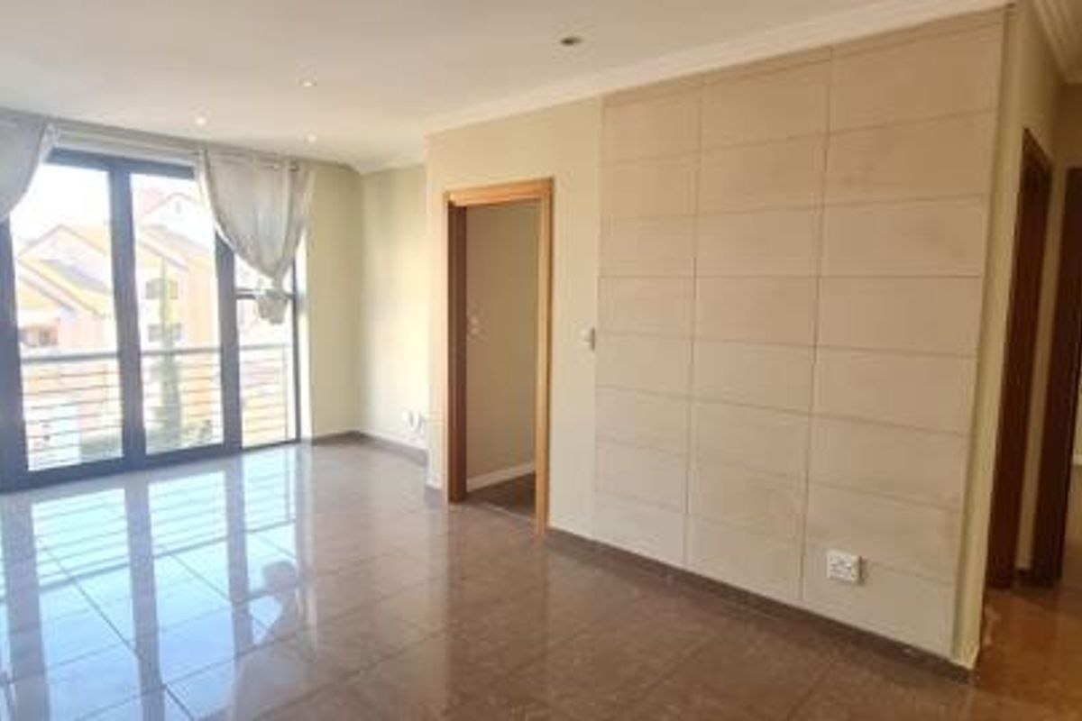 Spacious, light-filled living area featuring polished tiled floors, a modern feature wall, and large sliding doors leading to a balcony.