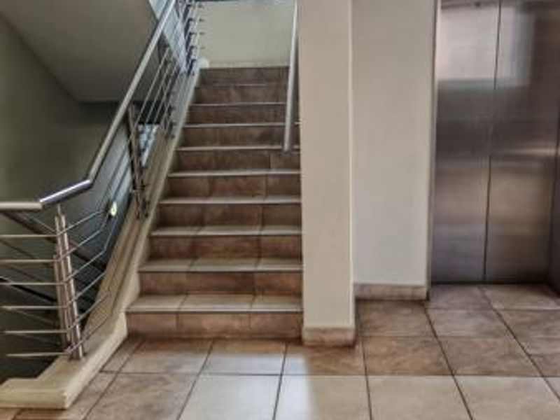 A clean, modern communal hallway featuring a tiled staircase with stainless steel balustrades and a built-in elevator for convenient access.