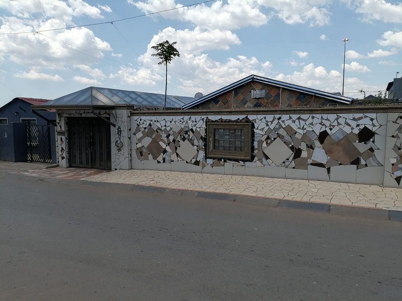 Front exterior view of a residential property featuring a distinctive mosaic-tiled boundary wall, metal security gate, and paved sidewalk area.