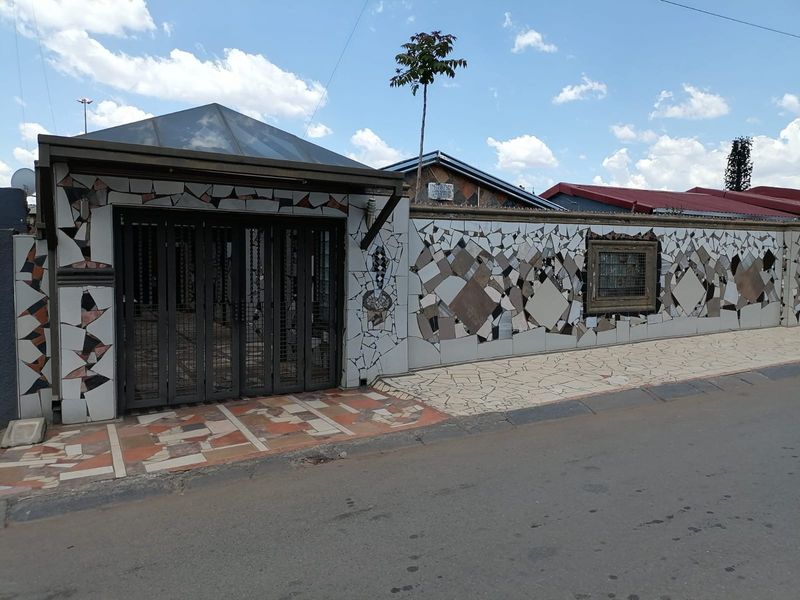 Front exterior view of the property featuring a distinctive mosaic-tiled boundary wall and a secure metal entrance gate.