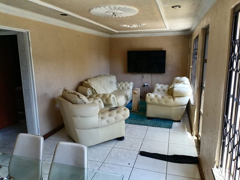A living room featuring ceramic floor tiles, decorative ceiling roses, and coving, with security gates installed on the windows.