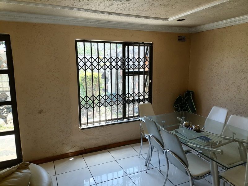 Dining room featuring tiled flooring, textured walls, decorative ceiling cornices, and a window fitted with a security gate.
