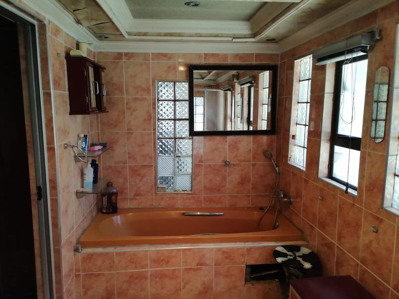 A dated bathroom featuring a built-in bathtub, glass block windows, and tiled walls, currently showing signs of ceiling water damage and missing paneling.