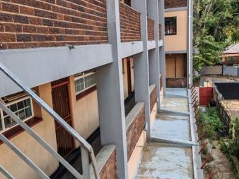 Exterior view of a multi-story commercial building featuring brick cladding, concrete walkways, and metal safety railings along the external access corridors.