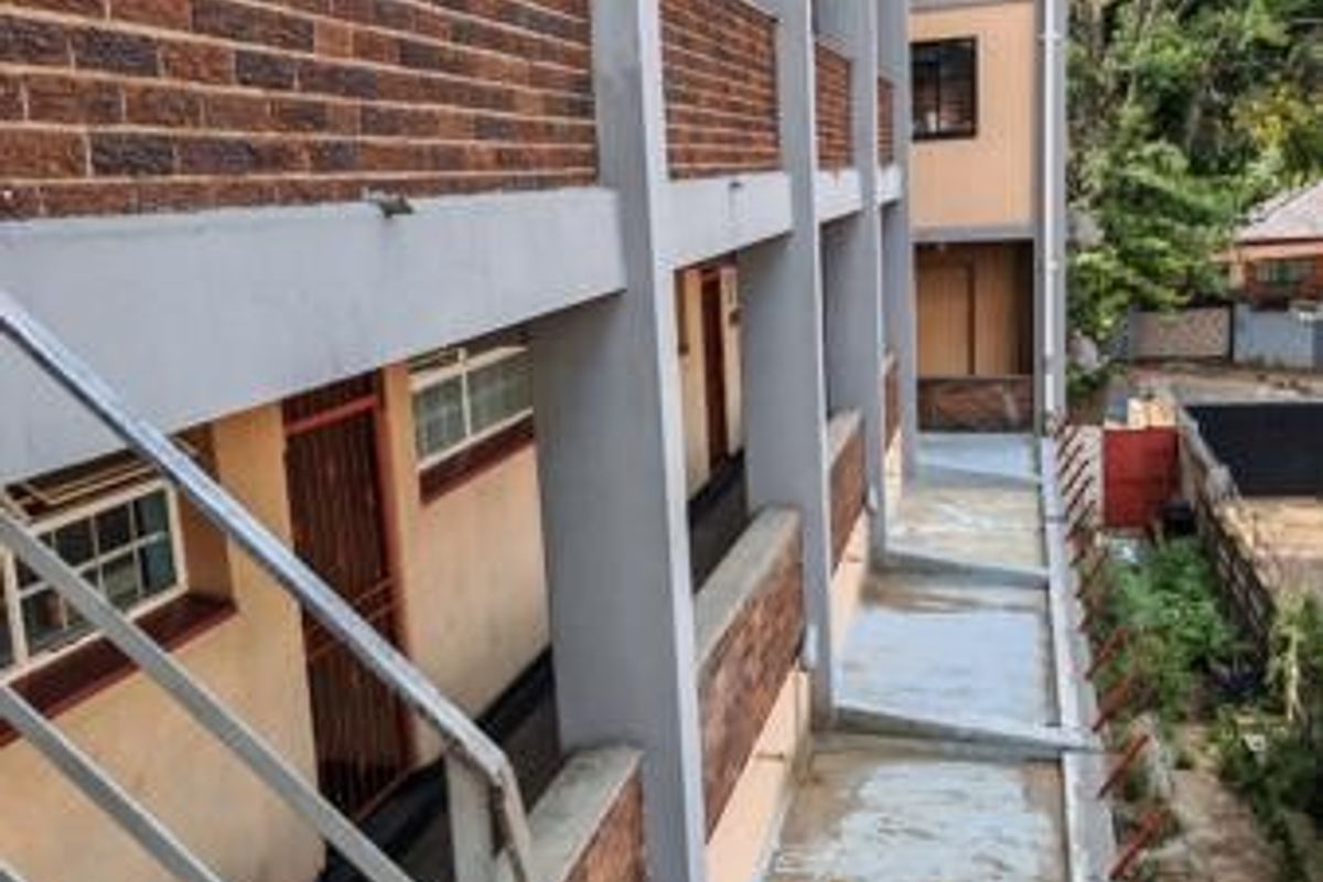 Exterior view of a multi-story commercial building featuring brick cladding, concrete walkways, and metal safety railings along the external access corridors.