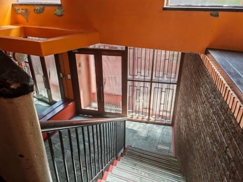 Entrance foyer featuring a staircase with metal balustrade, glass doors, security gate, and brick wall detailing, requiring cosmetic updates to the wall finishes.