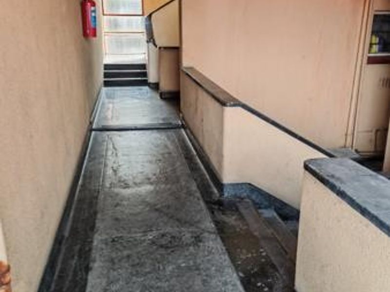 A functional commercial hallway featuring concrete flooring, a staircase, and wall-mounted fire safety equipment.