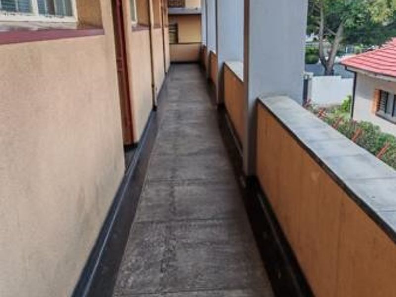An exterior covered walkway featuring concrete flooring, plastered walls, and a protective balustrade, providing access to the building's units.