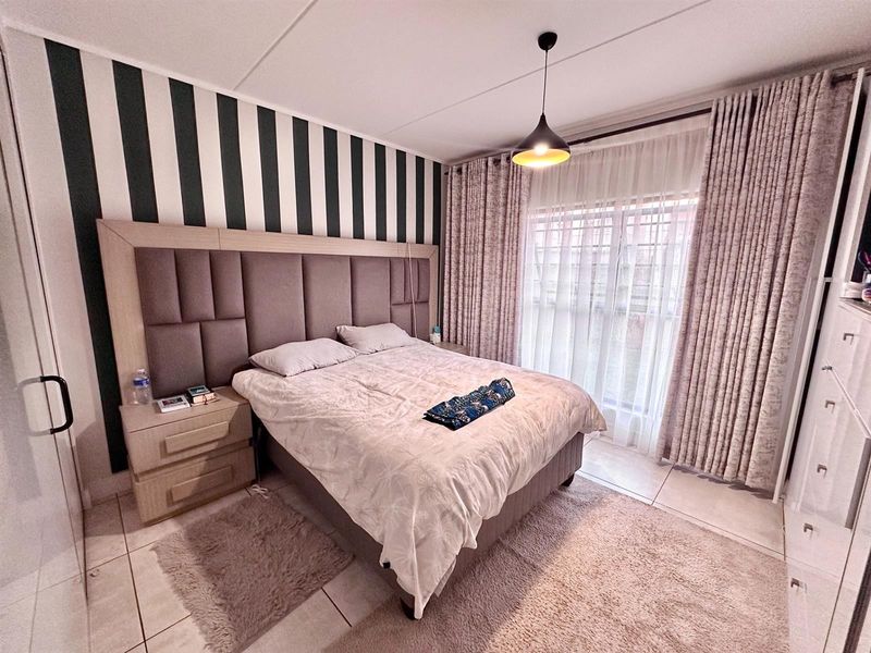 A well-maintained bedroom featuring tiled flooring, a modern pendant light, and a large sliding glass door with floor-to-ceiling curtains.