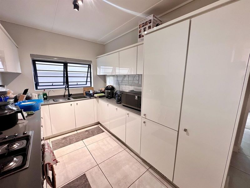 Modern kitchen featuring sleek white cabinetry, dark laminate countertops, a gas hob, and tiled flooring with a functional louvered window for ventilation.