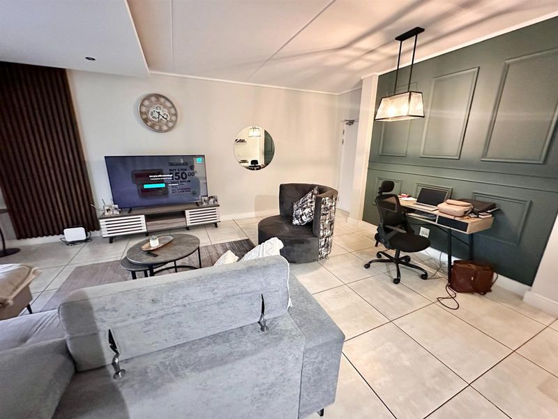 A well-maintained living area featuring large format floor tiles, decorative wall paneling, and modern recessed and pendant lighting.