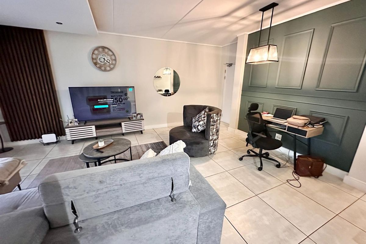 A well-maintained living area featuring large format floor tiles, decorative wall paneling, and modern recessed and pendant lighting.