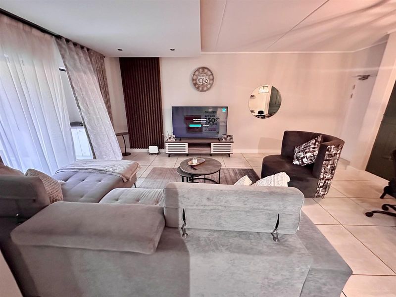 A well-maintained living room featuring neutral tiled flooring, recessed ceiling lighting, and decorative vertical wall paneling, creating a comfortable and functional living space.