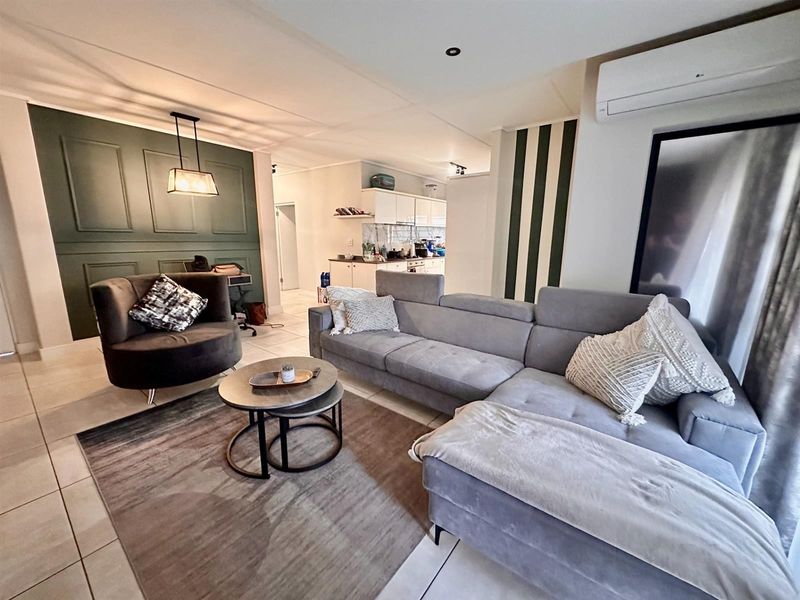 An open-plan living area featuring tiled floors, a decorative feature wall, and an integrated kitchen space with modern cabinetry and air conditioning.