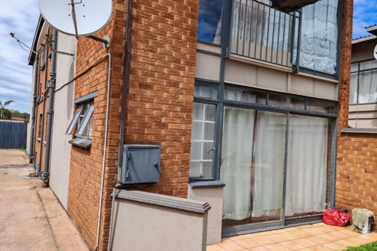 Rear exterior view of a multi-story commercial building featuring brick facade, sliding glass doors, a small tiled patio, and an upper-level balcony with metal railing.