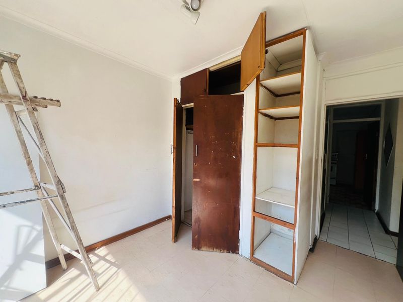 An empty bedroom featuring built-in cupboards with visible wear and tear, requiring cosmetic updates to restore its functionality and aesthetic appeal.
