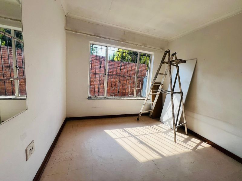 An empty bedroom featuring tiled flooring, security bars on the window, and neutral walls, currently undergoing minor maintenance.