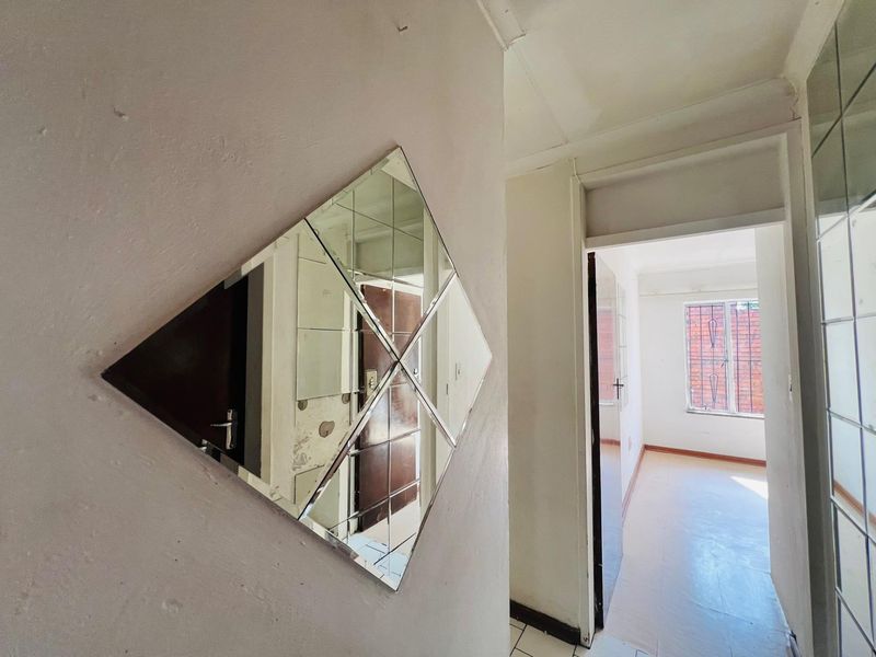 A vacant hallway featuring tiled flooring and access to an adjacent room with security-barred windows, requiring cosmetic updates to wall finishes.