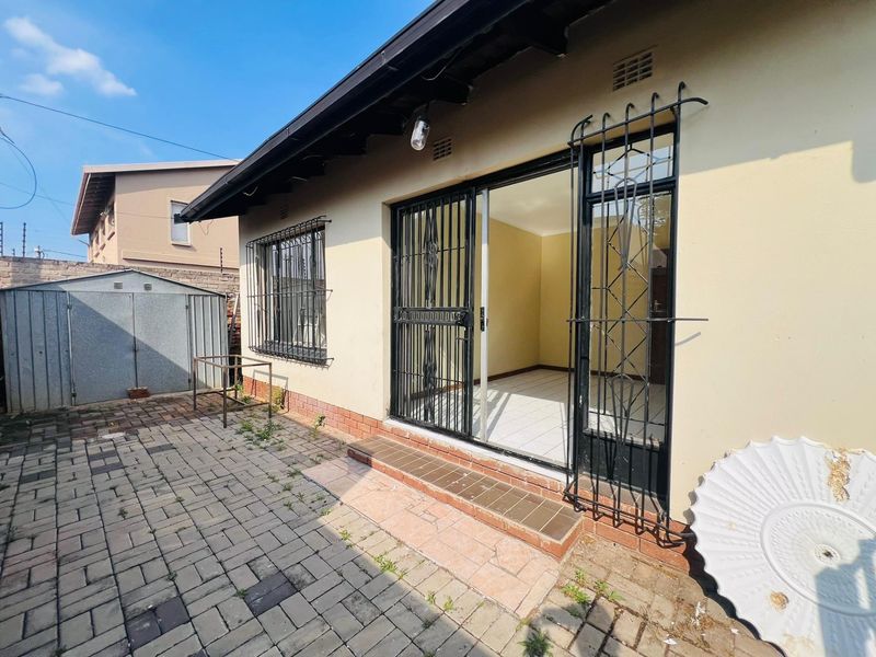 Rear exterior view featuring a paved patio area, security gates, and a metal garden shed.