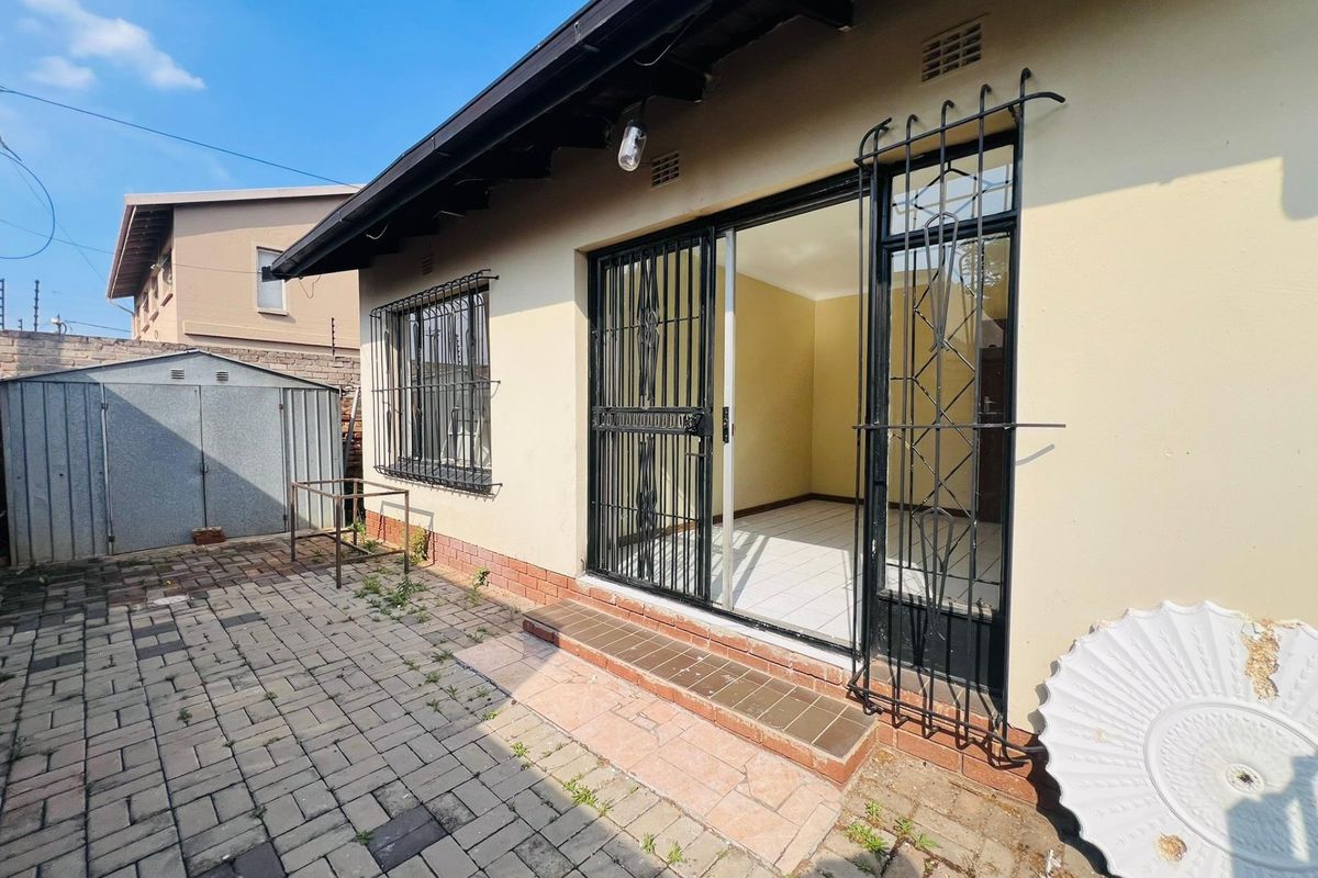 Rear exterior view featuring a paved patio area, security gates, and a metal garden shed.