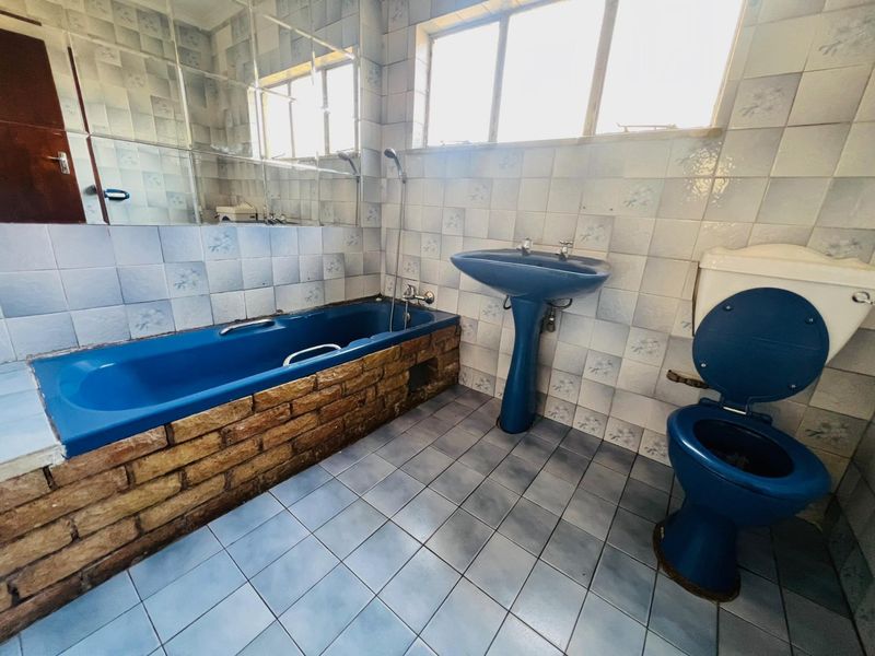 A dated bathroom featuring a blue suite, including a pedestal basin, toilet, and a brick-clad bathtub with tiled walls and flooring.