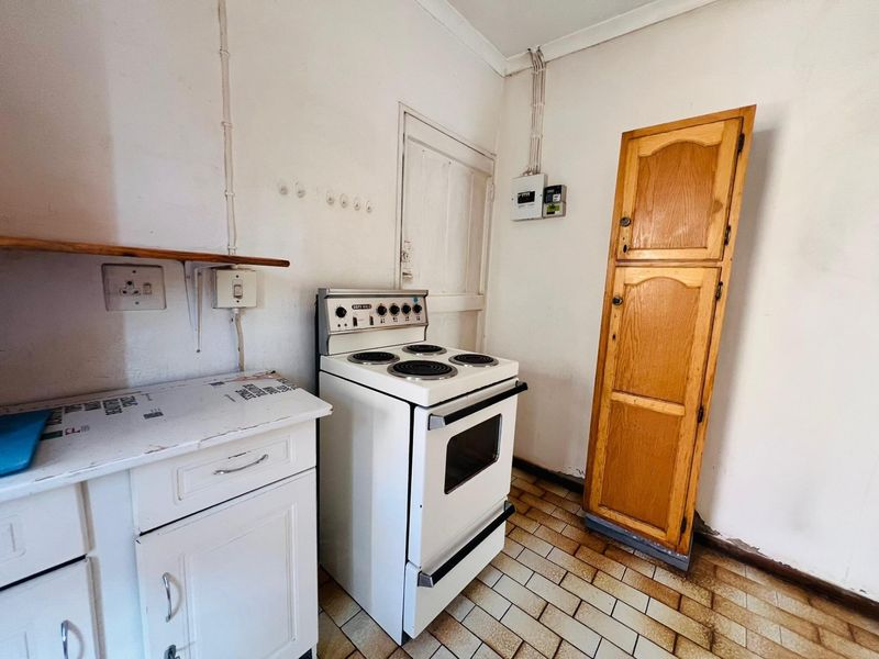 A functional kitchen area featuring a freestanding stove, built-in cabinetry, and tiled flooring, requiring cosmetic updates to modernize the space.