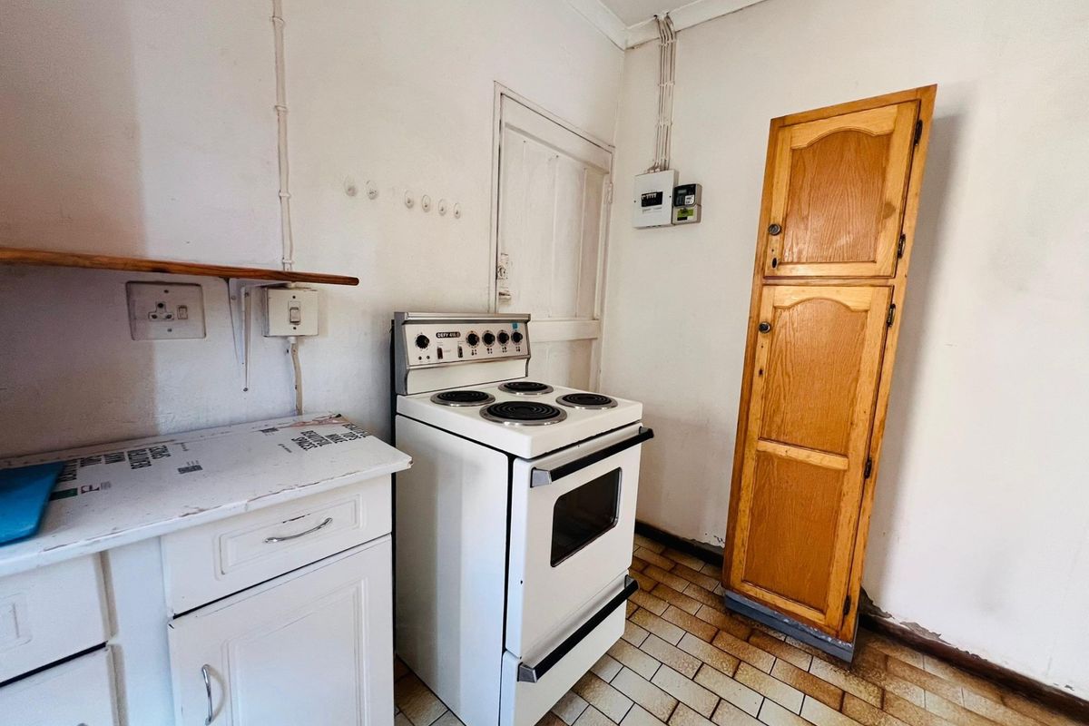 A functional kitchen area featuring a freestanding stove, built-in cabinetry, and tiled flooring, requiring cosmetic updates to modernize the space.