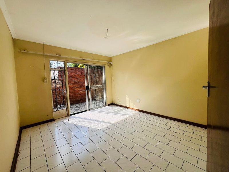 An empty living room featuring tiled flooring and a sliding glass door with security gate leading to an outdoor area.
