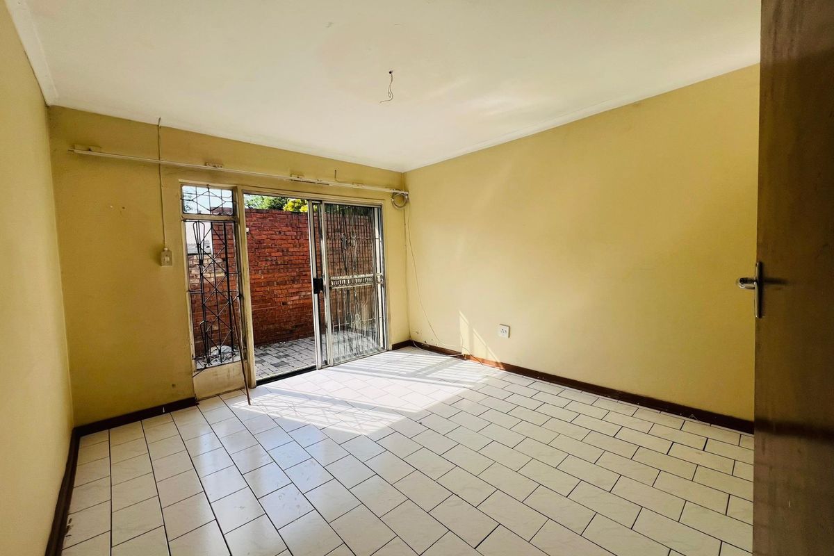 An empty living room featuring tiled flooring and a sliding glass door with security gate leading to an outdoor area.