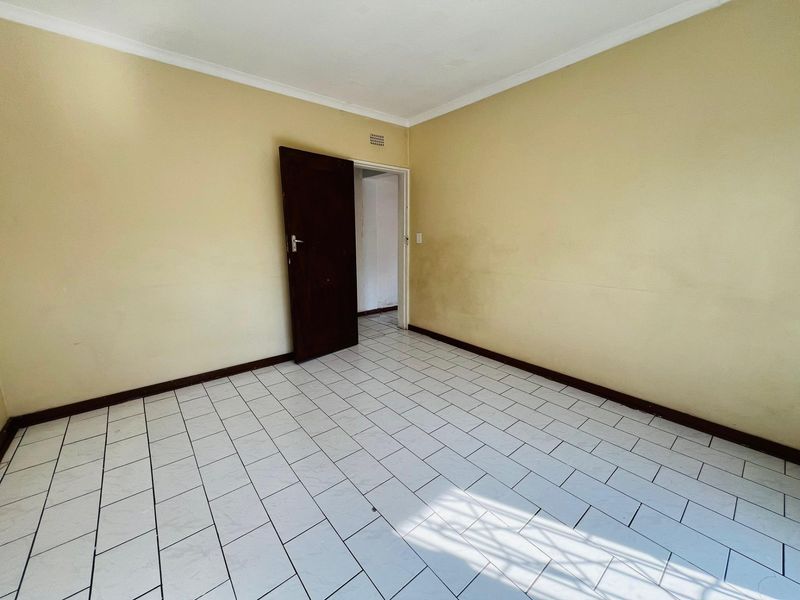 An empty bedroom featuring tiled flooring, neutral wall paint, and a single internal door, providing a blank canvas for renovation.