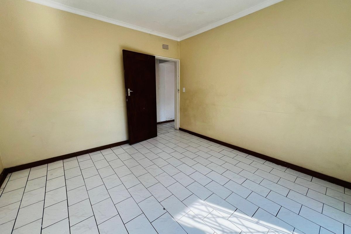 An empty bedroom featuring tiled flooring, neutral wall paint, and a single internal door, providing a blank canvas for renovation.