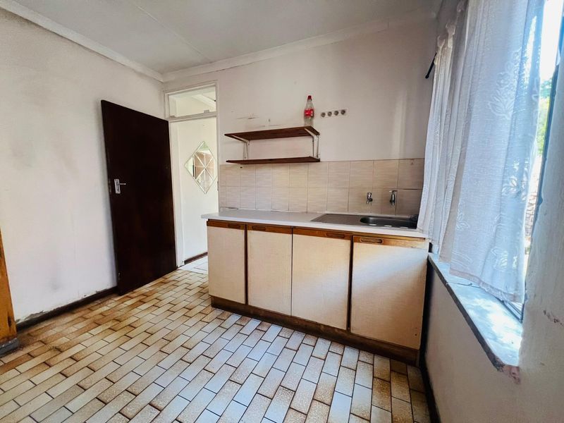 A dated kitchen area featuring built-in cabinetry, a stainless steel sink, tiled backsplash, and original tiled flooring, offering potential for modernization.