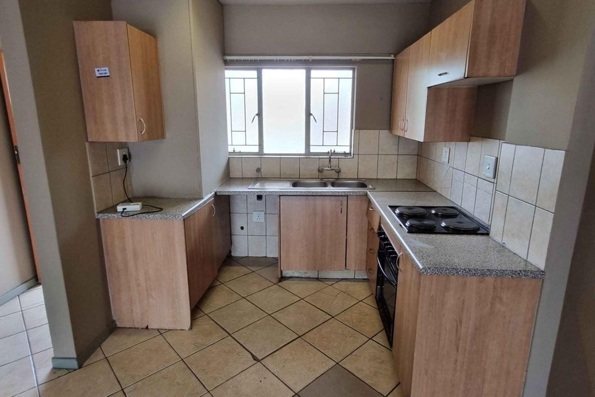 A functional kitchen featuring laminate cabinetry, stone-look countertops, a built-in oven and hob, and tiled flooring with a window providing natural light.