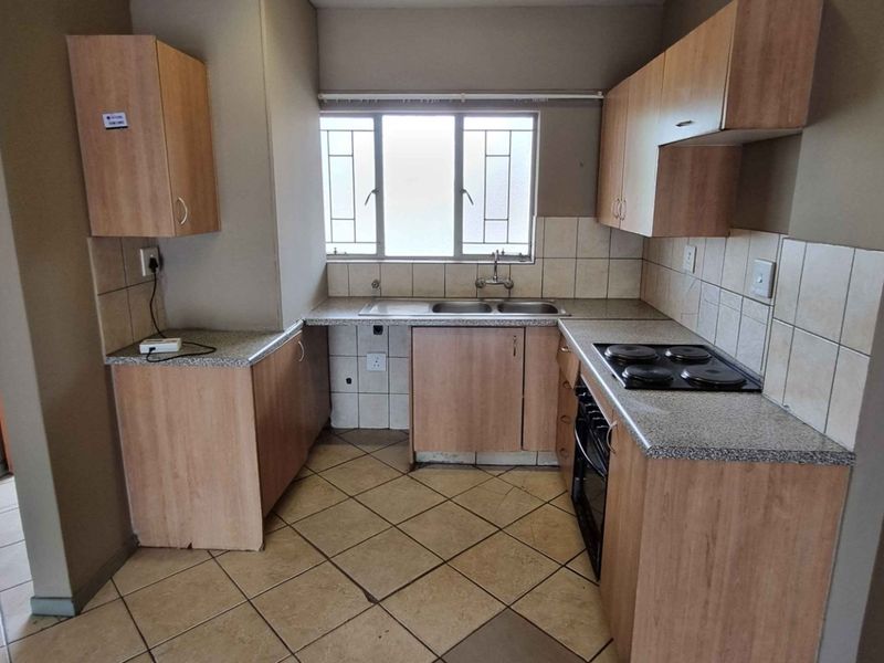 A functional kitchen featuring laminate cabinetry, stone-look countertops, a built-in oven and hob, and tiled flooring with a window providing natural light.
